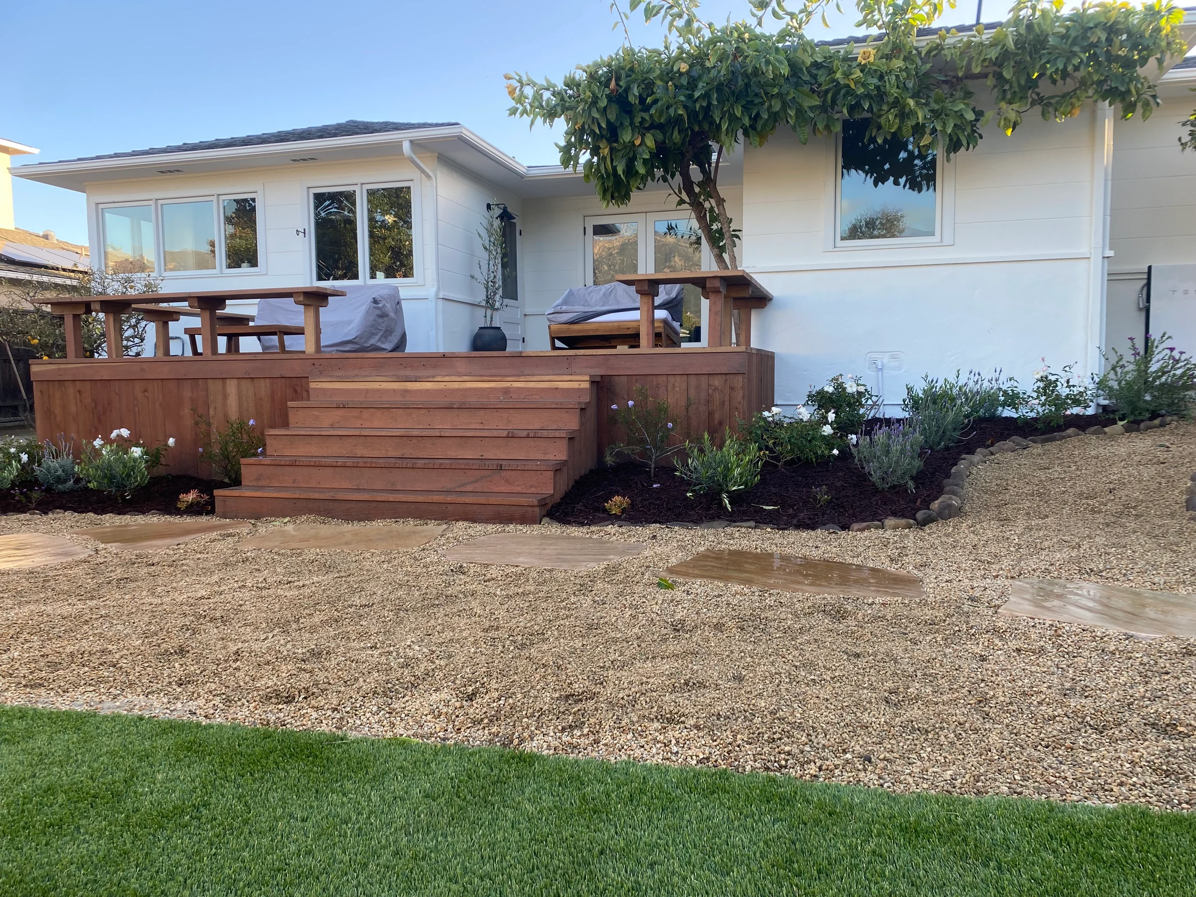 A timber deck and broad wooden steps connect a white house to its garden.